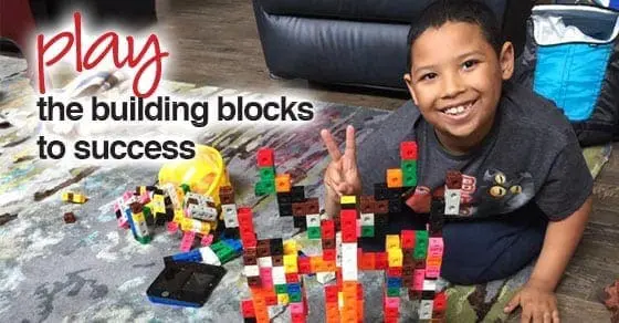 A young boy smiles and flashes a peace sign while playing with building blocks.