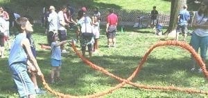 Children and adults play tug-of-war in a grassy area.