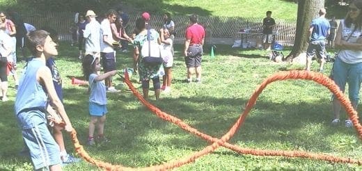Children and adults play tug-of-war in a grassy area.