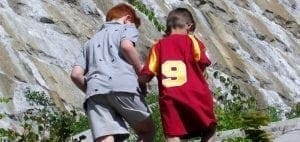 Two boys hold hands while facing a rocky cliff.