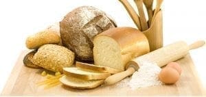 Various breads, baking tools, flour, and eggs on a wooden board