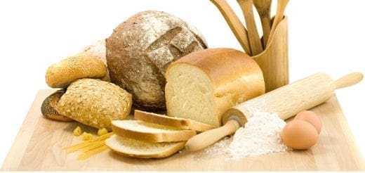 Various breads, baking tools, flour, and eggs on a wooden board