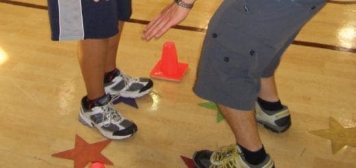 Two people's legs and feet on a wood floor with orange cones and star markers.