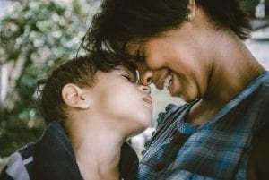 A woman and a child nuzzle their foreheads together, both smiling.