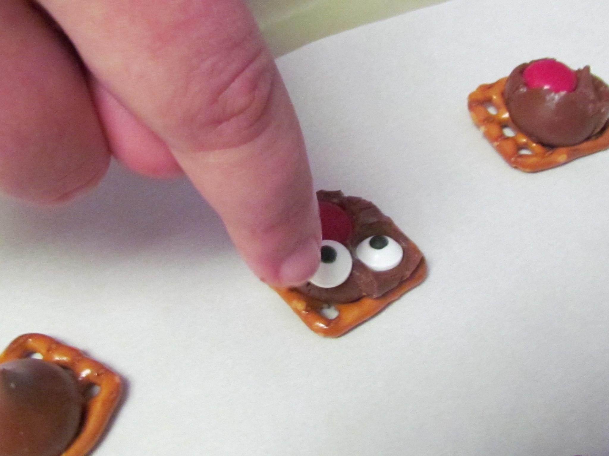 Finger pressing candy eyeballs onto a pretzel treat.