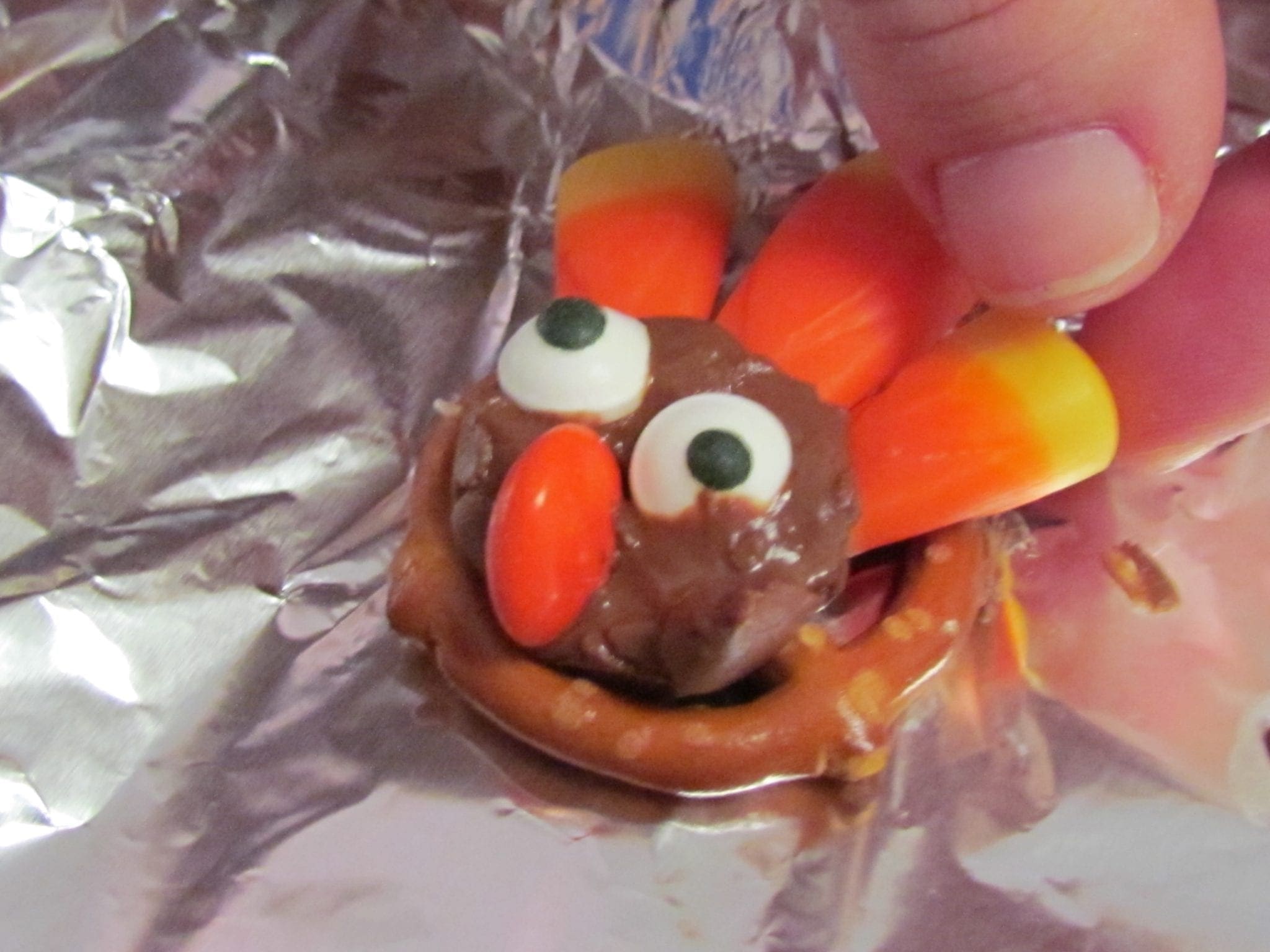 Hand decorating a pretzel treat to look like a turkey with candy corn and icing.