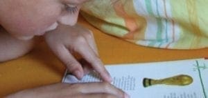 Child's hands point to text in a book with an illustration of a gold seal.