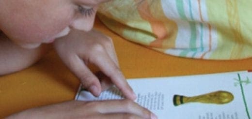 Child's hands point to text in a book with an illustration of a gold seal.