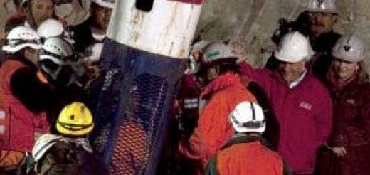 Group of people in hard hats gathered around a large cylindrical object.