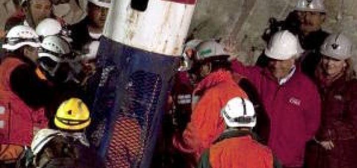 Group of people in hard hats gathered around a large cylindrical object.