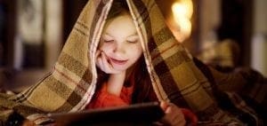 Young girl under a blanket using a tablet