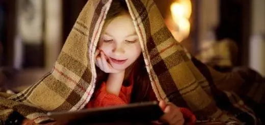 Young girl under a blanket using a tablet