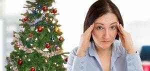 Woman with hands on temples near a Christmas tree.