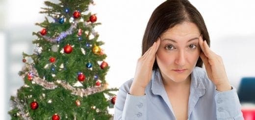 Woman with hands on temples near a Christmas tree.
