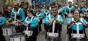 Drummers in matching turquoise and black uniforms playing in a parade.