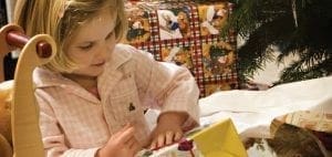 A young girl unwraps presents near a Christmas tree.