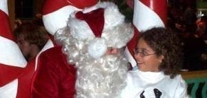 A child smiles next to a person dressed as Santa Claus.