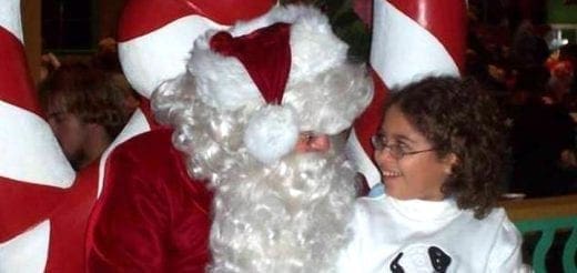 A child smiles next to a person dressed as Santa Claus.