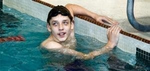 Young person in a swimming pool holding onto the edge.