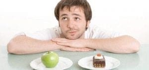 Man contemplating a choice between an apple and a piece of cake.