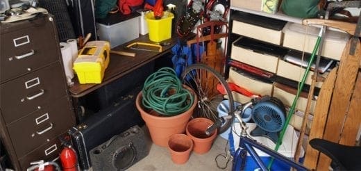A cluttered garage with a filing cabinet, tools, hoses, and storage boxes.