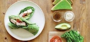 Green vegetable wraps on a plate beside avocado, lettuce, tomato, and dipping sauces.