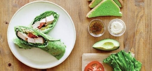 Green vegetable wraps on a plate beside avocado, lettuce, tomato, and dipping sauces.