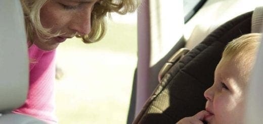 Woman leaning over to look at a baby in a car seat.
