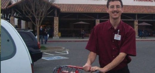 Young man in a maroon shirt with a name tag pushes a shopping cart.