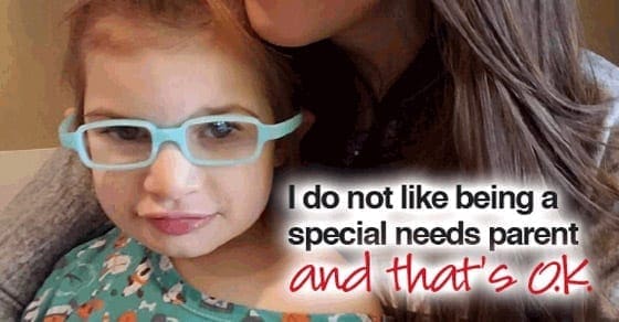 A young girl wearing light blue glasses is being hugged by an adult.