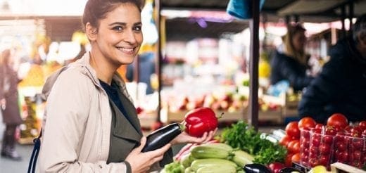 A smiling woman selects produce at an outdoor market.