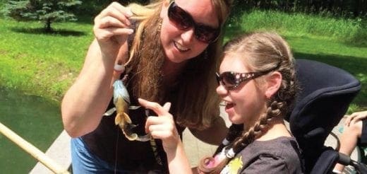 Shannon and Alyssa holding a small fish, winners of the "Mom & Me" 2016 Cover Contest.