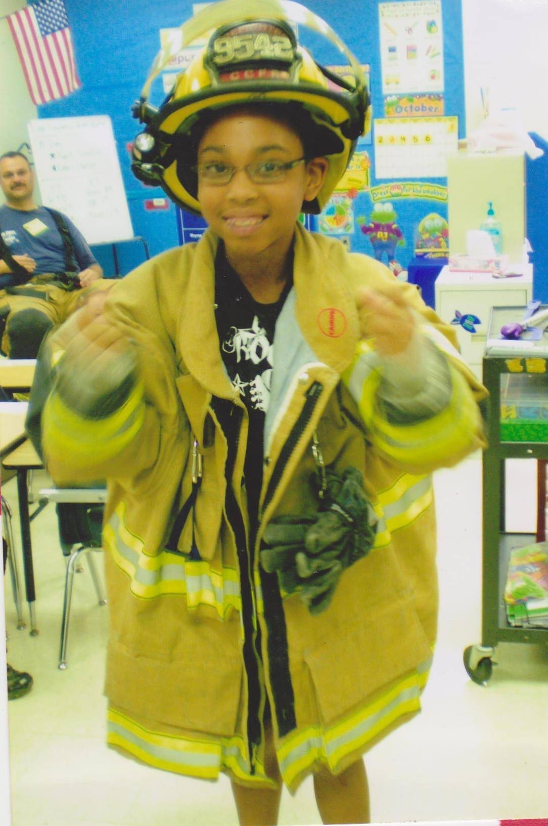 Child in firefighter costume with an American flag in the background.
