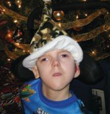 Jayden wearing a camouflage hat and a blue shirt in front of a Christmas tree.