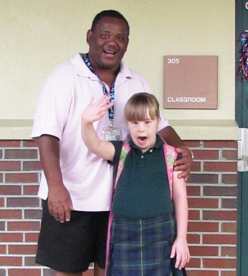 Lindsay Hires waves while standing with Rickey Smith Main in front of a classroom.
