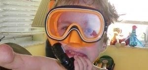 Child wearing an orange snorkel mask and breathing tube.