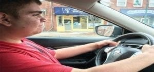 Matthew driving a car on a street.