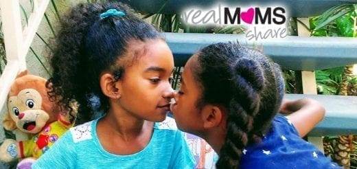 Two young girls, likely twins, share a tender moment.