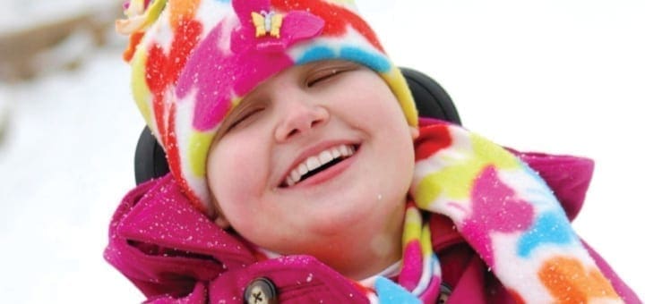 Cortney Kovack smiles while wearing a colorful hat and pink coat.