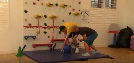 Two people interact with a medicine ball near a climbing wall.