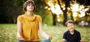 Woman meditating in a park with a boy in the background