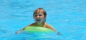 Child with a green inner tube in a pool.