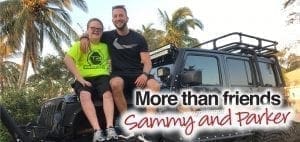 Sammy and Parker smile while sitting on a black jeep with palm trees in the background.
