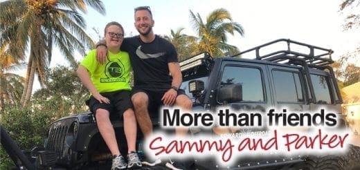 Sammy and Parker smile while sitting on a black jeep with palm trees in the background.