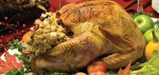 A golden-brown roasted turkey with stuffing, surrounded by fall decorations