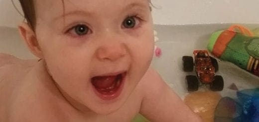 Baby smiling in a bathtub with toys.