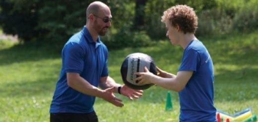 Two people in blue shirts are exercising outdoors with a medicine ball.