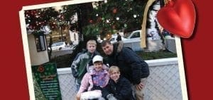 A family of four poses in front of a decorated Christmas tree.