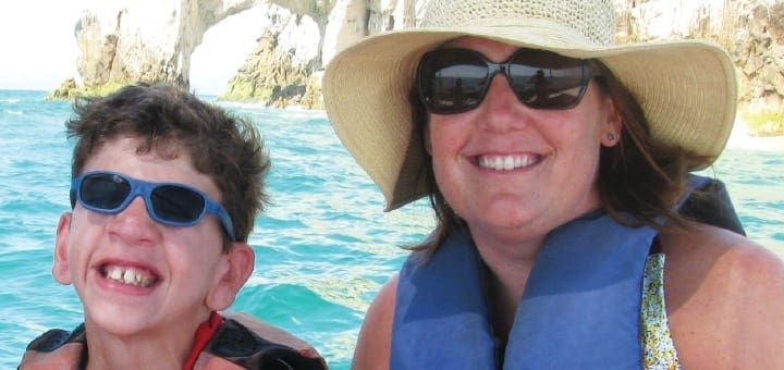 Beth Goddard wearing a sun hat and sunglasses, with a young boy also wearing sunglasses, on a boat.