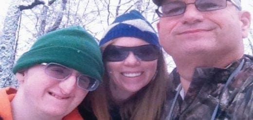 Three people in winter hats and sunglasses take a selfie outdoors.